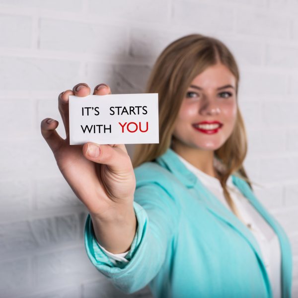 Motivational business quote. Business person in suit hold card with message. It Starts With You!